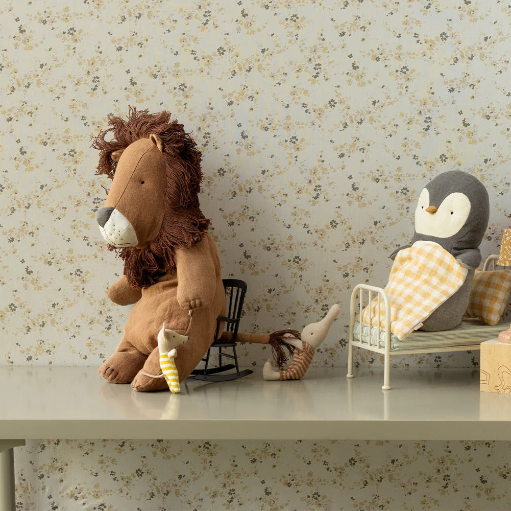 Stuffed lion and penguin toys on a shelf with a floral wallpaper background
