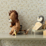 Stuffed lion and penguin toys on a shelf with a floral wallpaper background