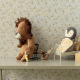Stuffed lion and penguin toys on a shelf with a floral wallpaper background